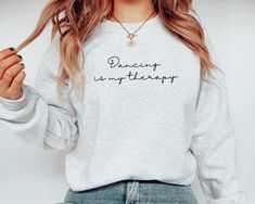 Find your peace on the dance floor with this "Dancing is My Therapy" sweatshirt. Perfect for dancers who view movement as a form of self-care, this cozy and stylish sweatshirt is a must-have for anyone who finds joy and relaxation through dance. Whether you're heading to class or just expressing your love for dance, this sweatshirt is the perfect way to showcase your passion. It also makes a thoughtful gift for dance lovers, instructors, or anyone who believes in the therapeutic power of dance. Hip Hop Long Sleeve Sweatshirt For Dance, Relaxed Fit Crew Neck Sweatshirt For Dance, Graphic Print Long Sleeve Sweatshirt For Dance, Dance Ministry, Dance Sweatshirt, Dancer Shirt, Find Your Peace, Ballerina Gift, Glitter Text