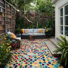 an outdoor living area with colorful rugs and plants on the ground, surrounded by bookshelves