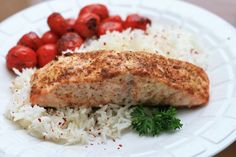 a white plate topped with meat and rice next to red tomatoes on top of a wooden table