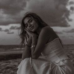 black and white photograph of a woman sitting on the beach with clouds in the background