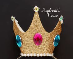 a gold crown with blue and pink jewels on it's side, against a black background