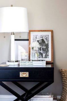 a black table topped with books next to a white lamp and pictures on the wall