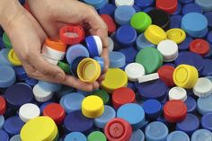 a person is picking up some colorful plastic caps from a bin filled with other containers