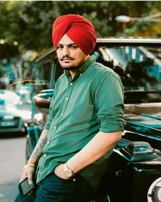 a man with a red turban sitting on the hood of a car