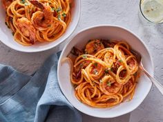 two white bowls filled with pasta and shrimp on top of a blue towel next to a glass of water