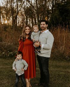 a man, woman and child posing for a photo in the grass with trees behind them