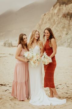 three bridesmaids standing on the beach with their bouquets in front of them