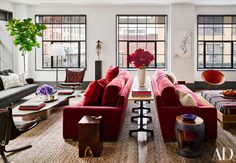 a living room filled with lots of furniture next to tall windows and plants in vases