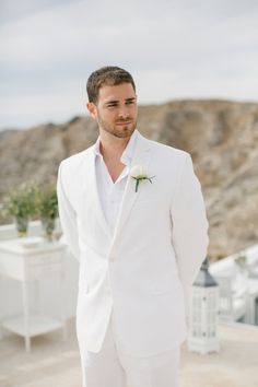 a man in a white suit and flower boutonniere standing on a roof