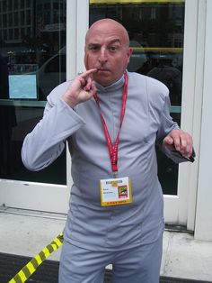 a man in grey suit standing next to a yellow caution tape and wearing a red lanyard around his neck