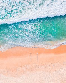 two people are standing on the beach in front of the ocean