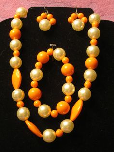 "The one of a kind, handmade jewelry set has multi shapes and sizes of  orange beads intermingled with 5/8\" cream color ball shaped beads.  The set has a 21\" long necklace, a 9\" long stretch bracelet and a paie of 2\" long pierced earrings.  Very unique addition for any wardrobe. FREE SHIPPING IN USA" Orange Jewelry Set, Handmade Jewelry Set, Heart Jewelry Set, Rabbit Jewelry, Orange Jewelry, Leather Phone Wallet, Aqua Beads, Gift Sets For Her, Plastic Jewelry