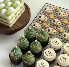 cupcakes with frosting and decorations are on a cooling rack next to a cake