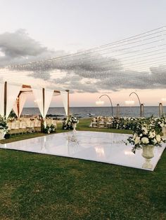 an outdoor wedding setup with white flowers and draping on the grass near the ocean