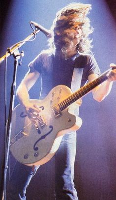 a man with long hair playing a guitar in front of microphones on stage at a concert