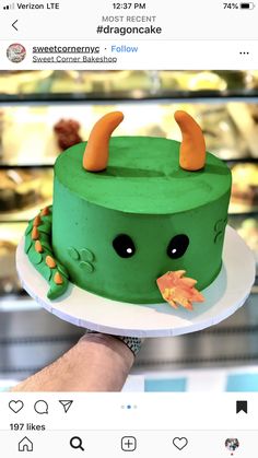 someone is holding a green cake with horns on it and an orange flower in the middle