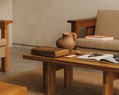 a wooden table topped with a book next to a chair and a vase on top of it