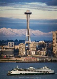 a large boat in the water near a city with snow capped mountains behind it,