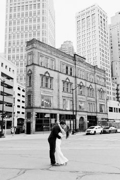 a bride and groom kissing on the street in front of tall buildings