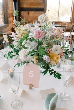 the table is set with white and pink flowers, greenery, candles and place cards