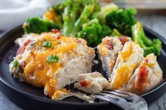 a black plate topped with broccoli and chicken covered in cheesy cheese