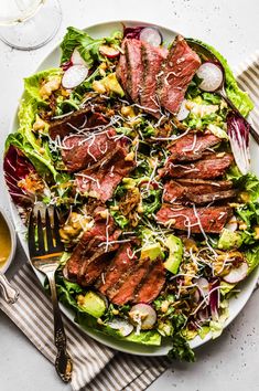 a plate with steak and salad on it next to a glass of wine, silverware and utensils