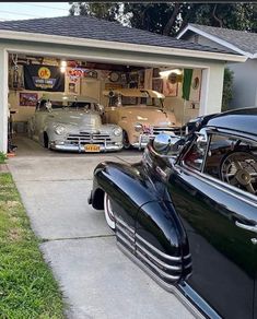 two classic cars parked in front of a garage with their doors open and the hood up