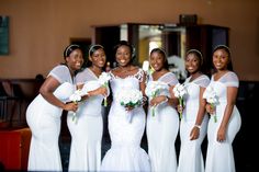 a group of women standing next to each other wearing white dresses and holding bouquets