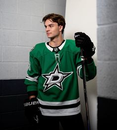 a man in green jersey holding a hockey stick and wearing black gloves with white stars on it