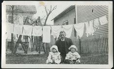 an old black and white photo of two children in front of a house with laundry hanging on the clothesline