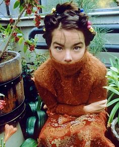 a woman sitting on top of a wooden bench next to potted plants