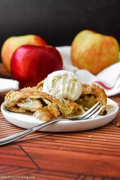 a white plate topped with apple pie next to two pieces of fruit on a wooden table