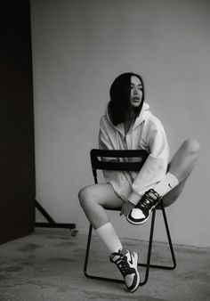 a woman sitting in a chair with her legs crossed and wearing converses on the ground