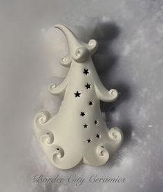 a white ceramic christmas tree ornament with stars on it's side in the snow