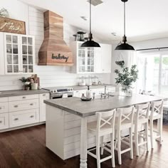 a large kitchen with white cabinets and wooden flooring, an island table surrounded by chairs