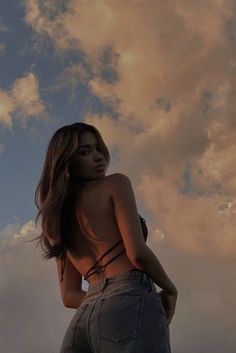 a woman standing on the beach with her back to the camera and clouds in the background