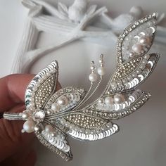 a close up of a person holding a brooch with pearls and leaves on it