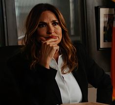 a woman sitting at a desk with her hand on her chin and looking off to the side