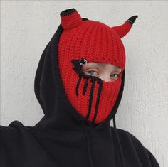 a person wearing a red and black knitted devil mask with horns on their head