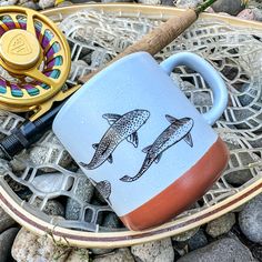 a fishing rod and two mugs sitting on some rocks next to a fish hook