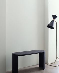 a black table sitting in front of a white wall next to a lamp and floor lamp