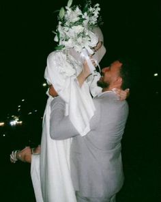 a man holding a woman in his arms and flowers on her head while she smiles