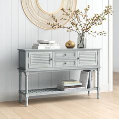 a console table with books and vases on it in front of a white wall