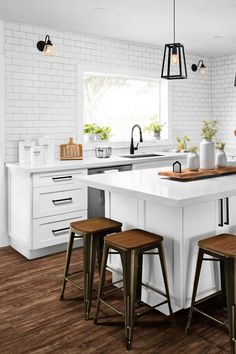 a white kitchen with wooden stools next to an island