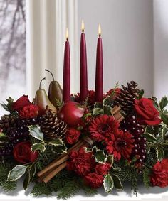 a christmas centerpiece with candles, apples and other holiday decorations in red flowers on a white table