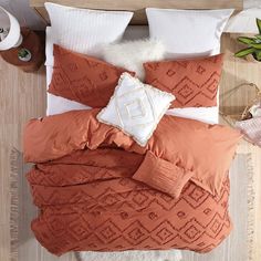 a bed with an orange comforter and pillows on top of it next to a potted plant