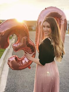 a woman is holding some balloons in the shape of an number 3 and smiling at the camera