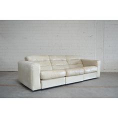 a white leather couch sitting on top of a cement floor next to a brick wall