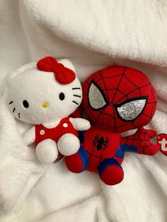 hello kitty and spider - man stuffed animals are laying on a white bed sheet together