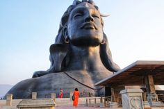 there is a large statue in front of a building with people standing around it and looking up at the sky